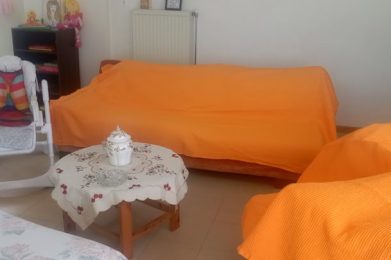 Ανθρώπινο εσωτερικό με δύο καναπέδες καλυμμένους με πορτοκαλί καλύμματα και παιδική καρέκλα, σε οικι.